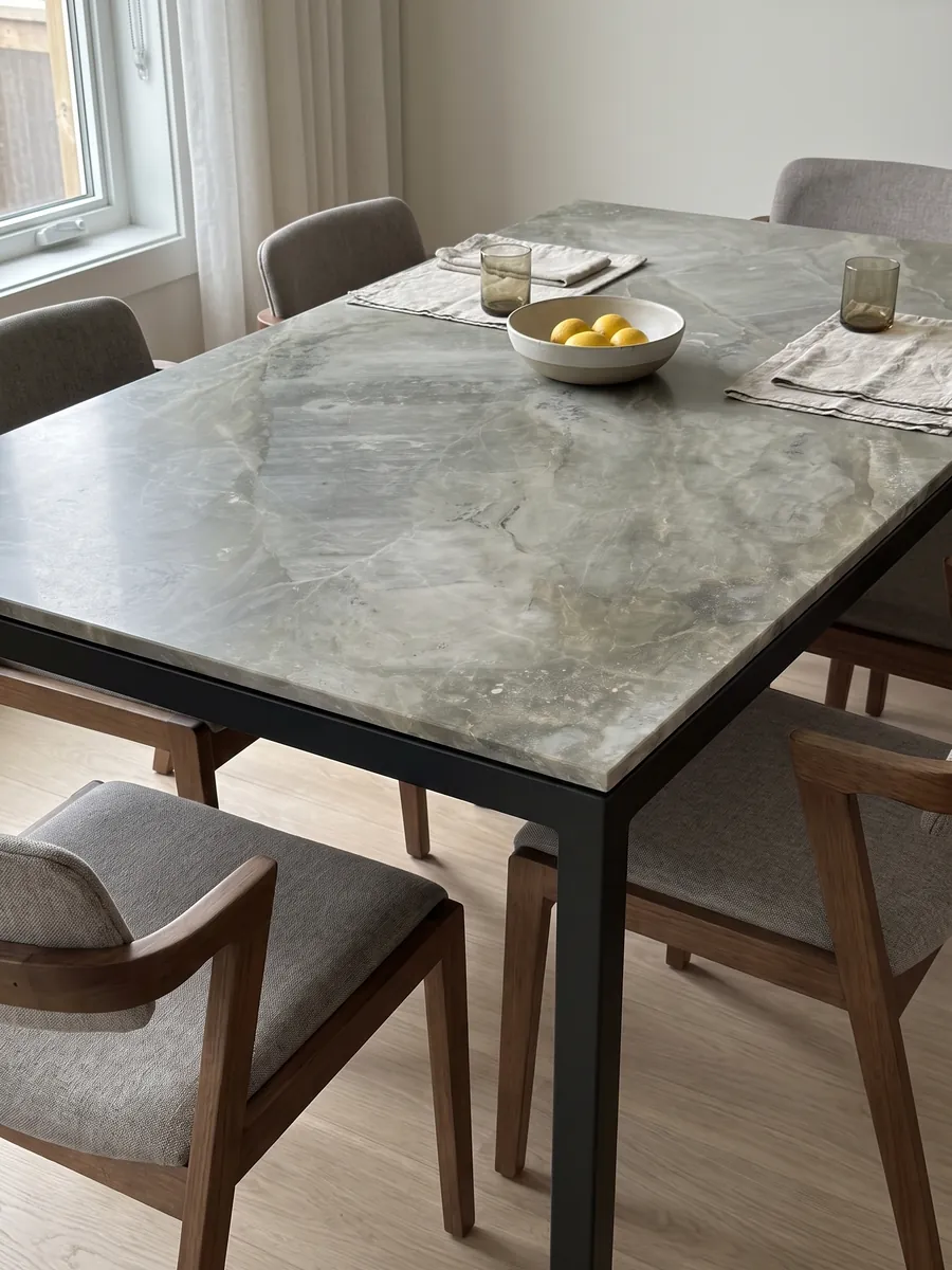 Mesa de comedor con cubierta de mármol gris Fior di Bosco sobre base de acero: gris verdoso apagado con nubes tonales y vetas finas casi invisibles