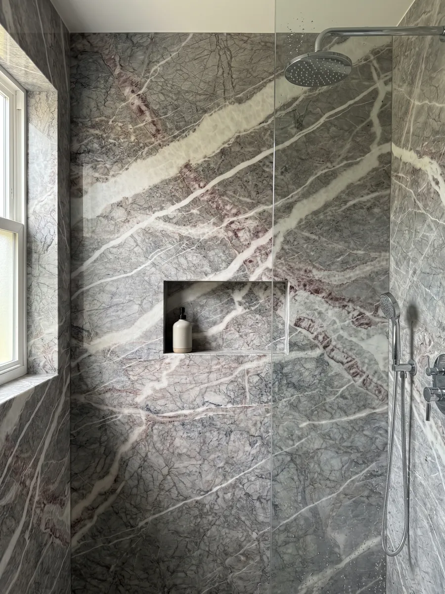 Ducha revestida con placas enteras de mármol gris Fior di Pesco Carnico con nicho empotrado: vetas blancas diagonales acompañadas de vetas color vino sobre gris con red de líneas finas