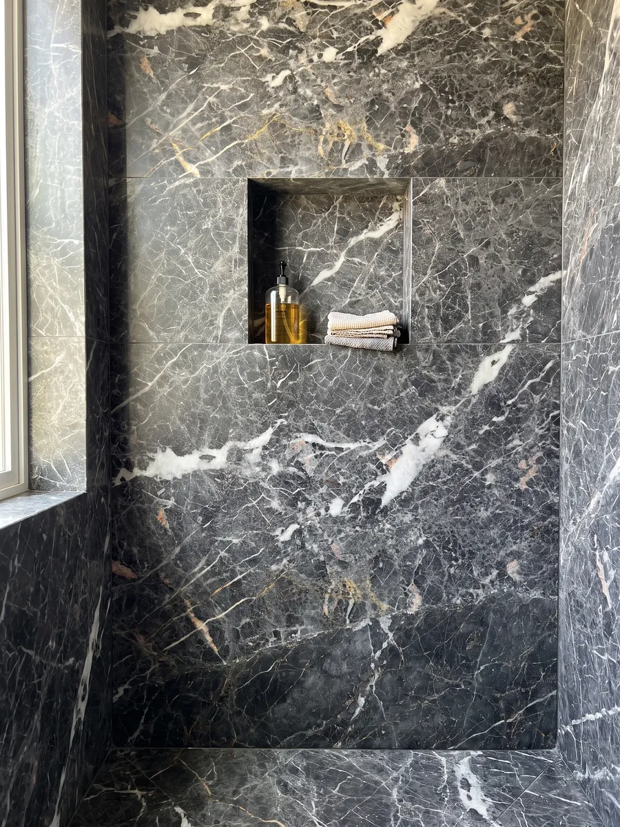 Ducha revestida con placas enteras de mármol gris Grey Saint Laurent con nicho empotrado: gris oscuro con manchas blancas alargadas y una red fina de vetas claras y doradas