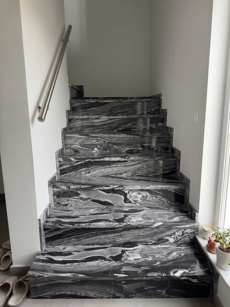 Escalera interior con peldaños de Mármol Gris Imperial con pasamanos: ondas horizontales grises y blancas sobre negro, como corrientes en movimiento