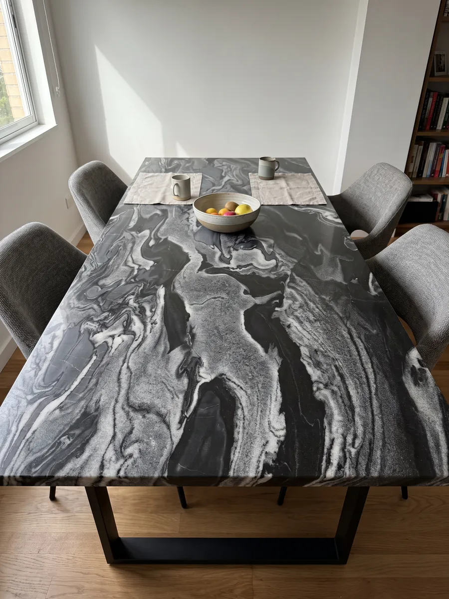 Mesa de comedor con cubierta de Mármol Gris Imperial sobre base de acero: ondas horizontales grises y blancas sobre negro, como corrientes en movimiento