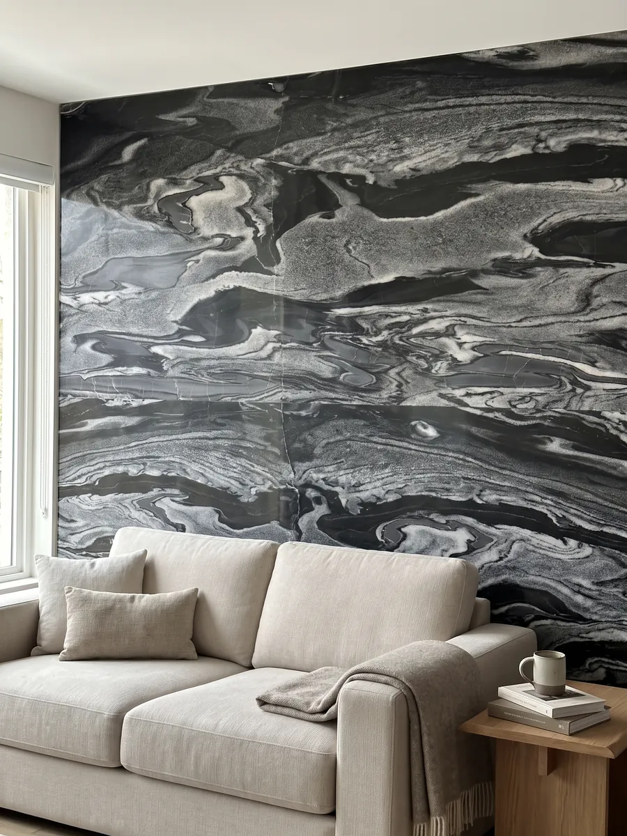 Pared de sala revestida con placas de Mármol Gris Imperial abiertas en libro detrás de un sofá: ondas horizontales grises y blancas sobre negro, como corrientes en movimiento