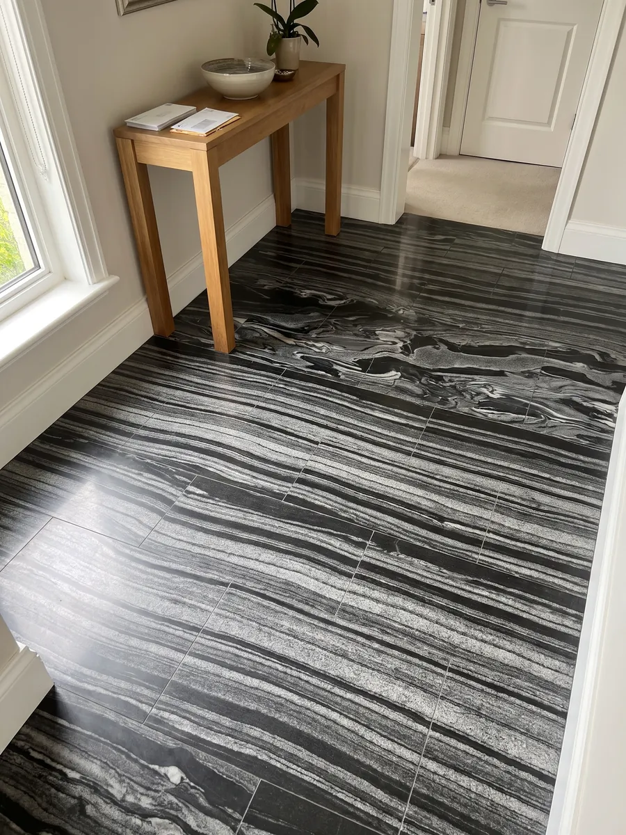 Piso de recibidor en placas grandes de Mármol Gris Imperial con luz natural: ondas horizontales grises y blancas sobre negro, como corrientes en movimiento