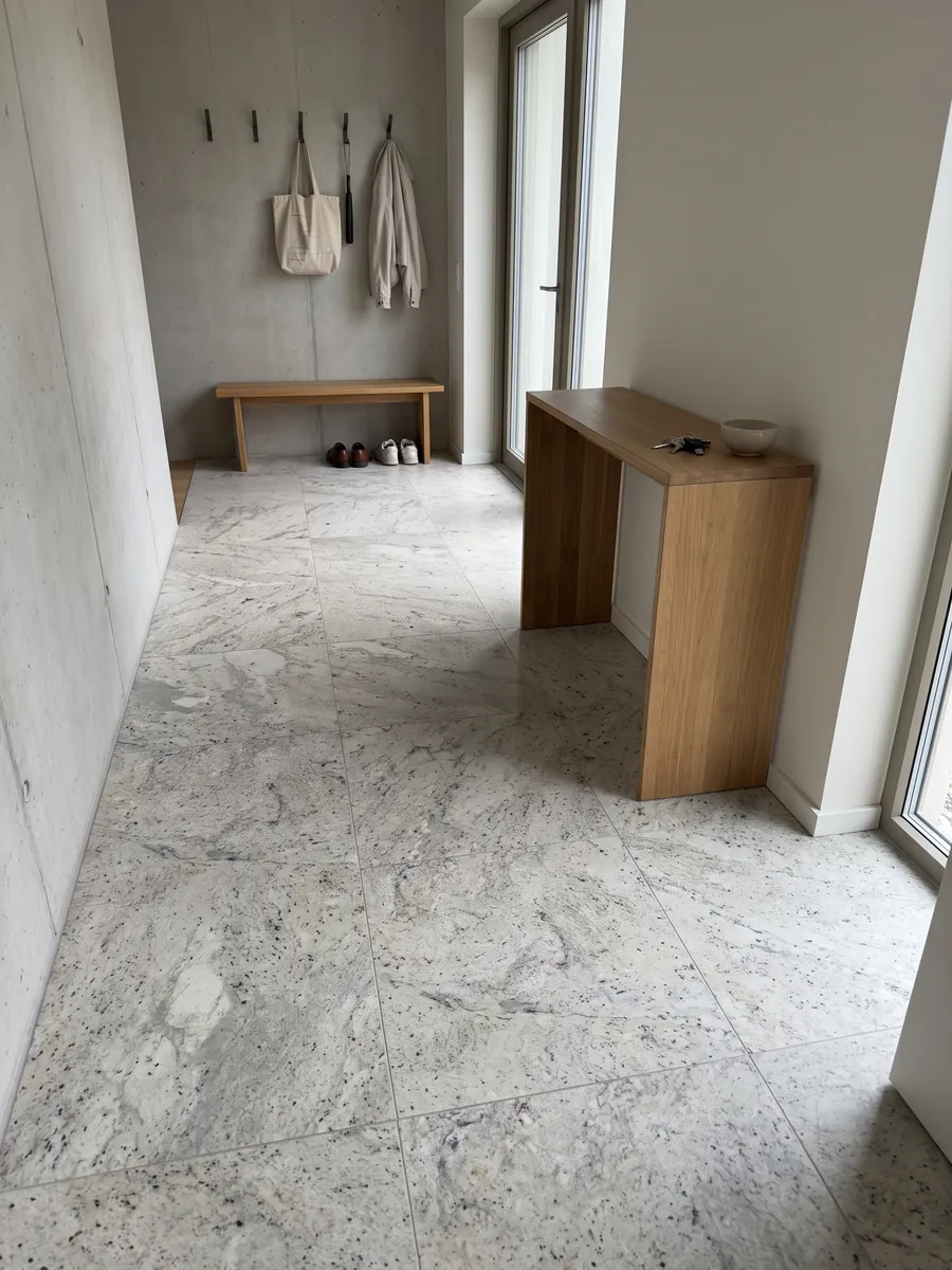 Piso de recibidor en placas grandes de mármol gris Lemon Ice con luz natural: gris claro salpicado de motas oscuras, con aspecto parecido al granito
