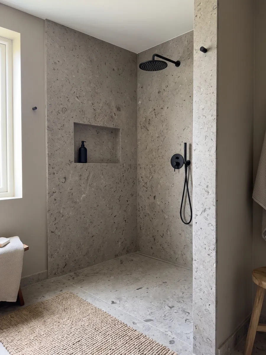 Ducha revestida con placas enteras de mármol gris Lipica Fiorito con nicho empotrado: gris beige con pequeñas figuras fósiles oscuras repartidas por toda la placa