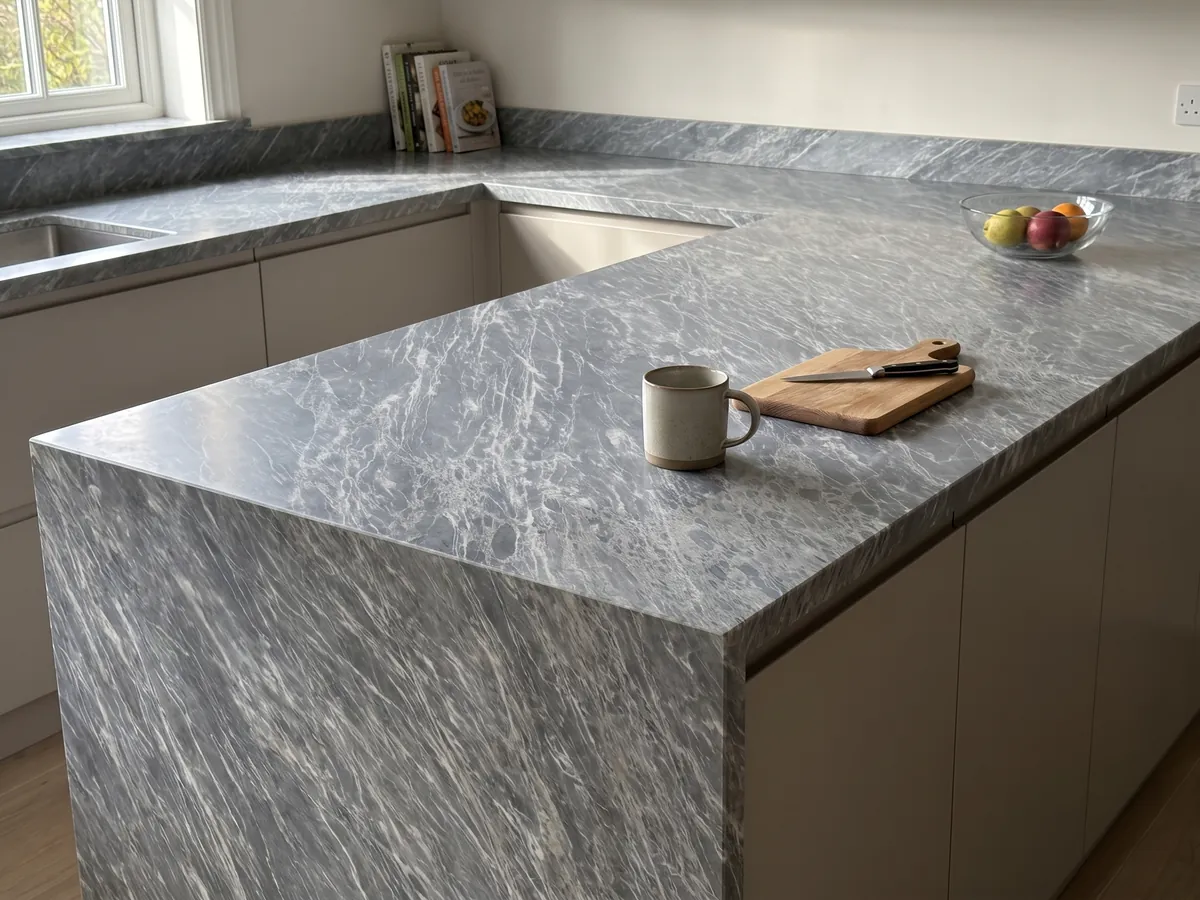 Isla de cocina con cubierta de Mármol Gris Perla y canto recto en una cocina con luz natural: gris azulado cubierto de trazos blancos finos y paralelos en diagonal
