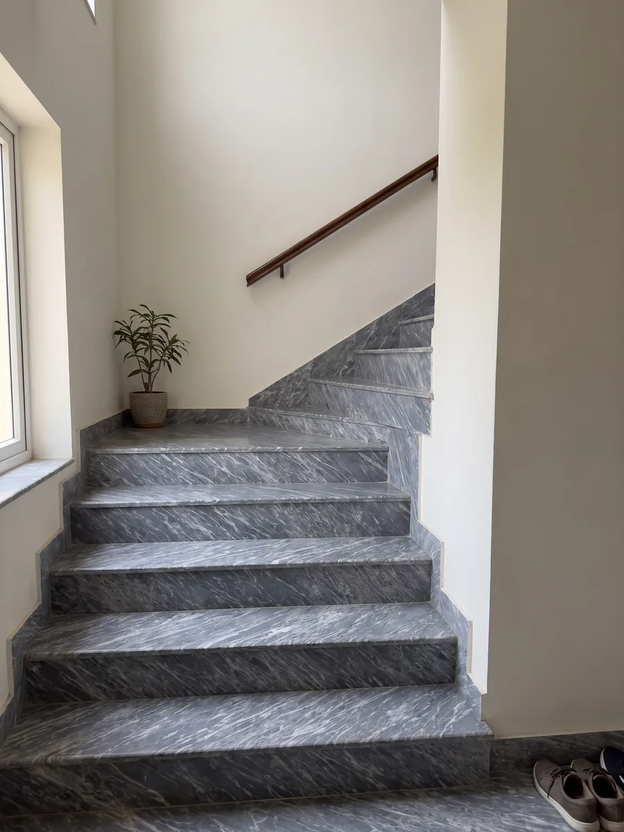 Escalera interior con peldaños de Mármol Gris Perla con pasamanos: gris azulado cubierto de trazos blancos finos y paralelos en diagonal