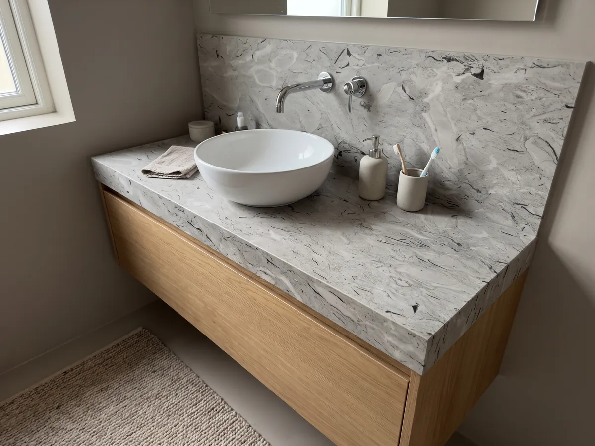 Cubierta de lavabo y pared de baño en mármol gris Repen con lavamanos blanco y grifería cromada: gris claro con trazos negros curvos de fósiles y nubes horizontales