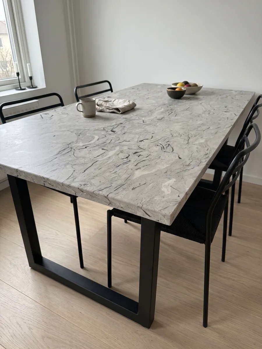 Mesa de comedor con cubierta de mármol gris Repen sobre base de acero: gris claro con trazos negros curvos de fósiles y nubes horizontales