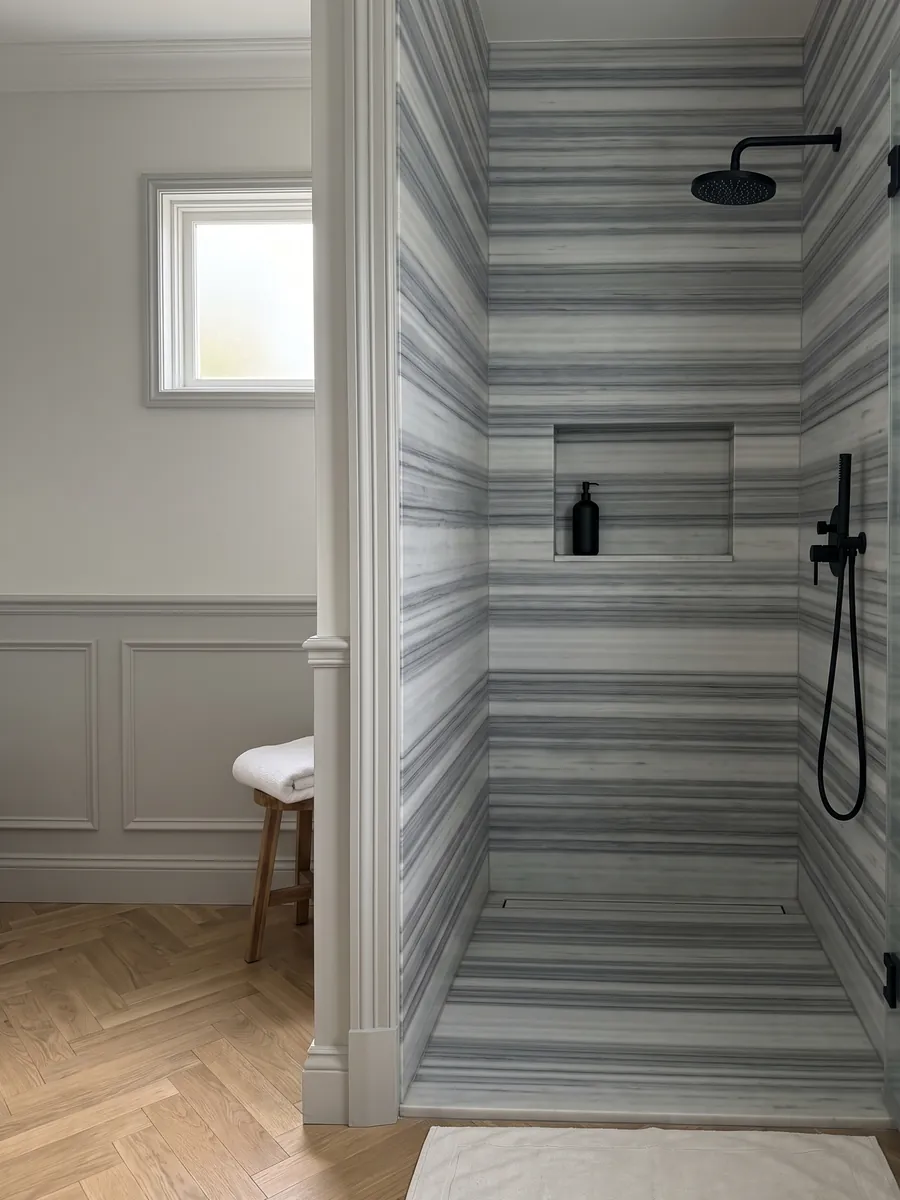 Ducha revestida con placas enteras de mármol gris Striato Olimpico con nicho empotrado: franjas horizontales perfectamente paralelas en tonos gris azulado y blanco, como rayas continuas