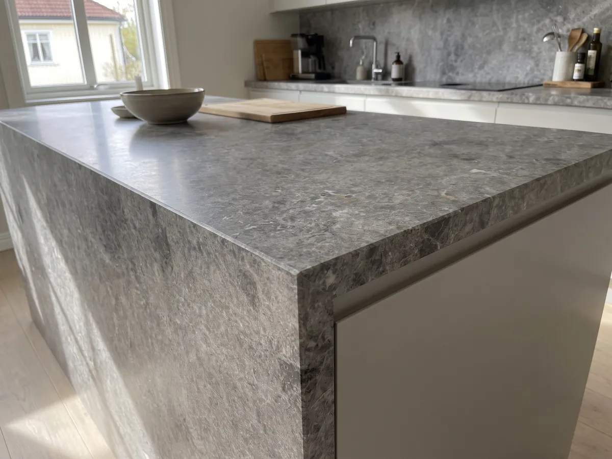 Isla de cocina con cubierta de mármol gris Tundra y canto recto en una cocina con luz natural: gris medio con nubes más oscuras y salpicado fino de puntos claros