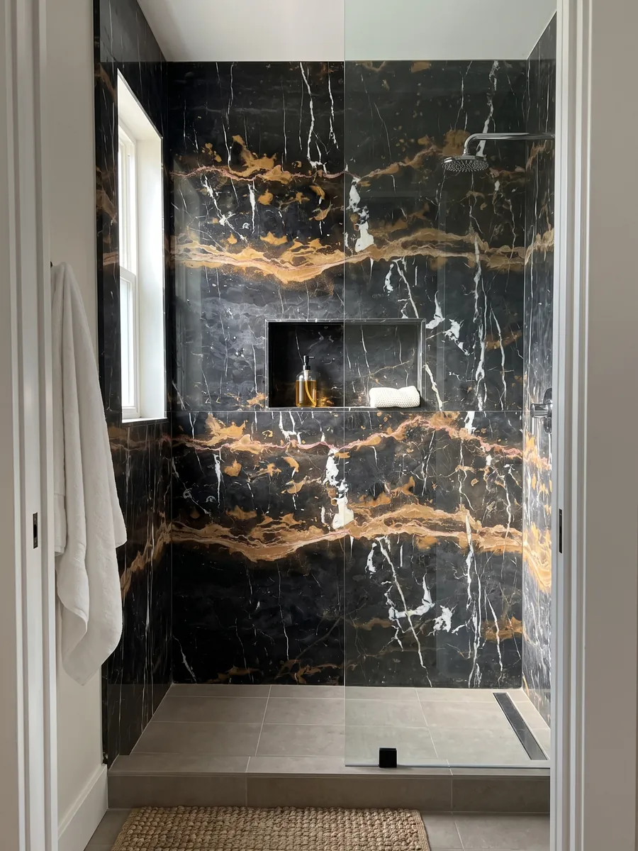 Ducha revestida con placas enteras de mármol negro Black & Gold con nicho empotrado: negro con dos bandas horizontales ocre dorado y vetas blancas verticales