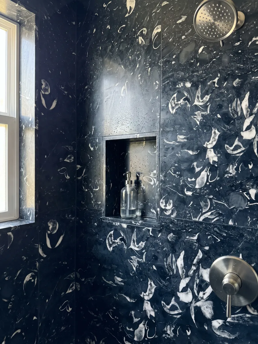 Ducha revestida con placas enteras de Mármol Negro Boreale con nicho empotrado: negro azulado con conchas fósiles blancas curvas bien visibles