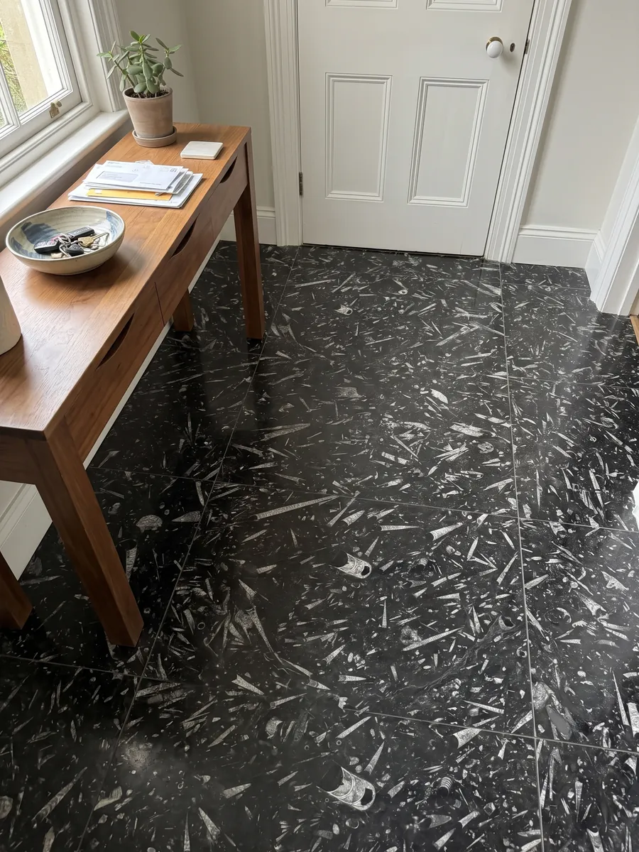 Piso de recibidor en placas grandes de mármol negro Fossil Black con luz natural: fondo negro lleno de fósiles alargados en forma de cono, de color gris claro