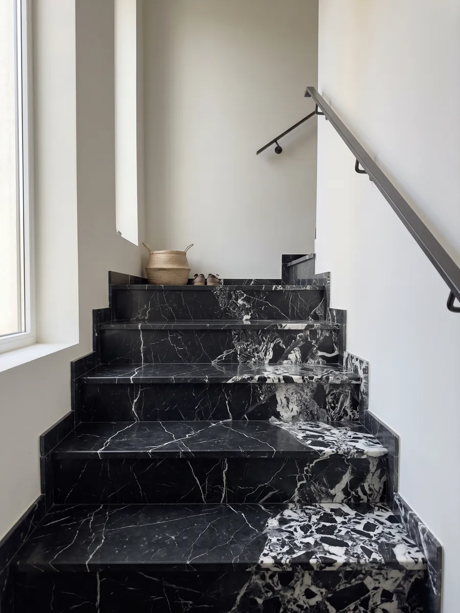 Escalera interior con peldaños de mármol negro Grand Antique con pasamanos: negro intenso con una zona de fragmentos blancos rotos que ocupa un lado de la placa