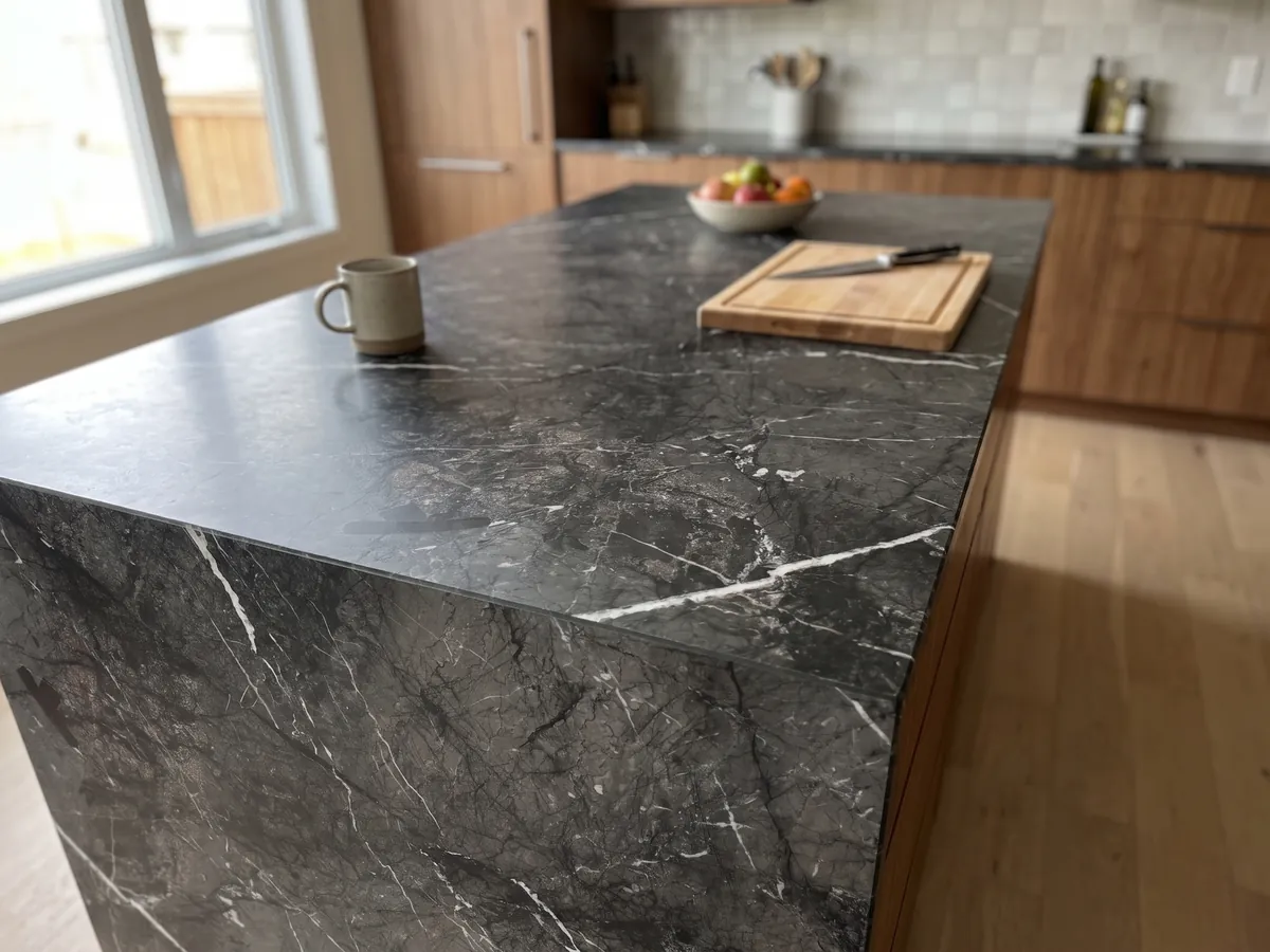 Isla de cocina con cubierta de mármol negro Grigio Carnico y canto recto en una cocina con luz natural: negro grisáceo con vetas blancas finas y nítidas que se ramifican