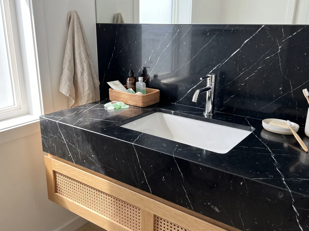 Cubierta de lavabo y pared de baño en mármol negro Nero Marquina con lavamanos blanco y grifería cromada: negro profundo con pocas vetas blancas finas y rectas