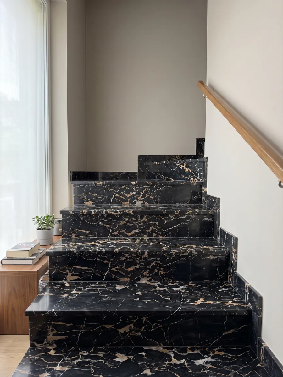 Escalera interior con peldaños de mármol negro Nero Portoro con pasamanos: negro con una red densa de vetas doradas y blancas