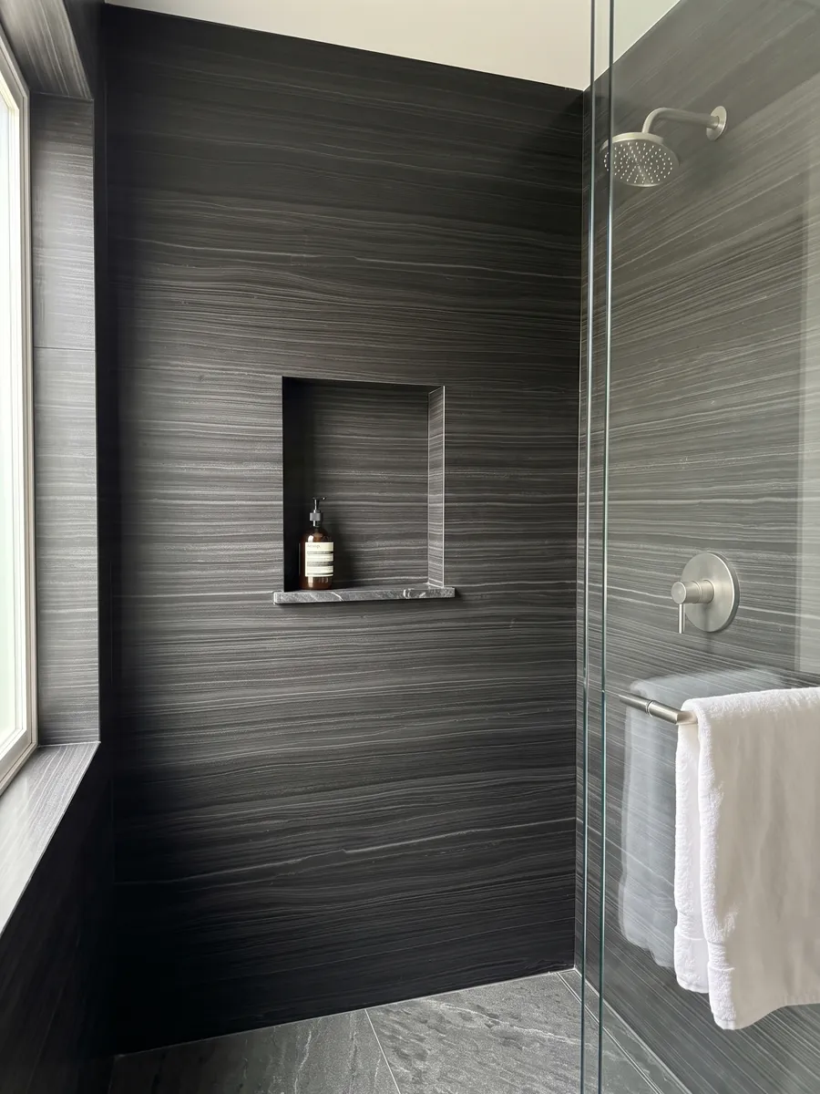 Ducha revestida con placas enteras de Mármol Negro Pagoda con nicho empotrado: negro con finas líneas grises horizontales y paralelas, casi como madera