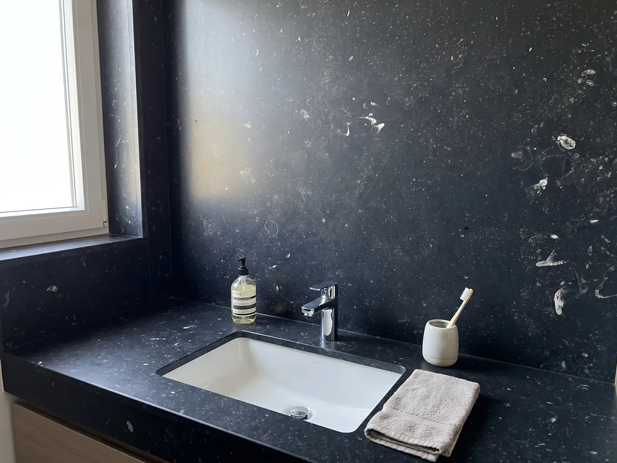 Cubierta de lavabo y pared de baño en mármol negro Pierre Bleu con lavamanos blanco y grifería cromada: negro azulado con pequeñas motas claras dispersas