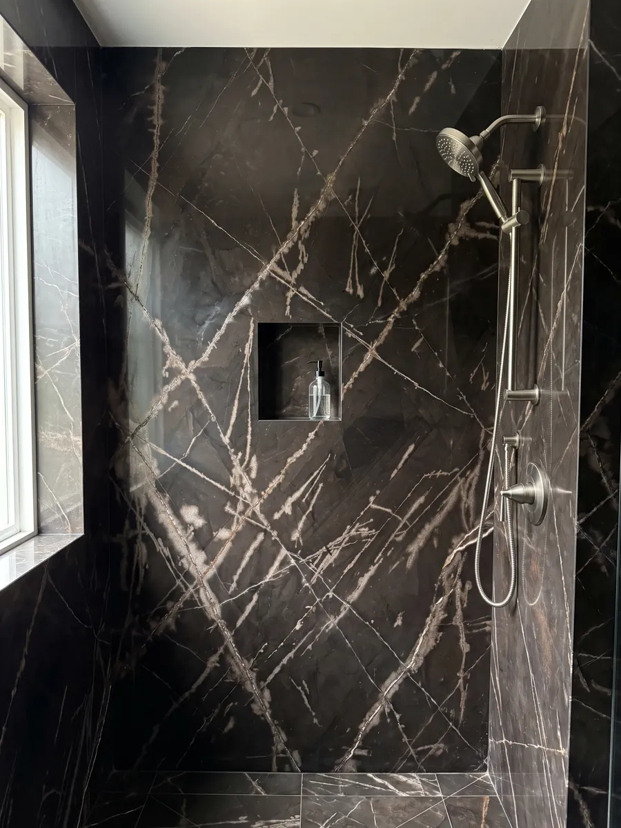 Ducha revestida con placas enteras de mármol negro Sahara Bronze con nicho empotrado: fondo negro amarronado con vetas color bronce finas y cruzadas