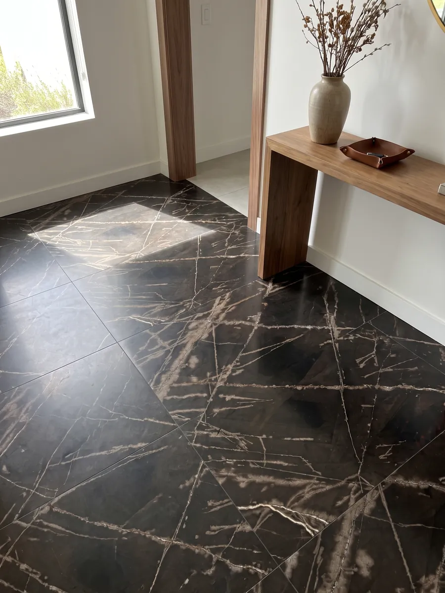 Piso de recibidor en placas grandes de mármol negro Sahara Bronze con luz natural: fondo negro amarronado con vetas color bronce finas y cruzadas