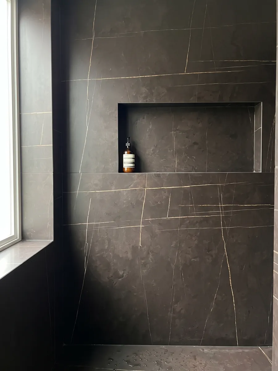 Ducha revestida con placas enteras de mármol negro Sahara Noir con nicho empotrado: negro amarronado con líneas doradas muy finas, rectas y escasas