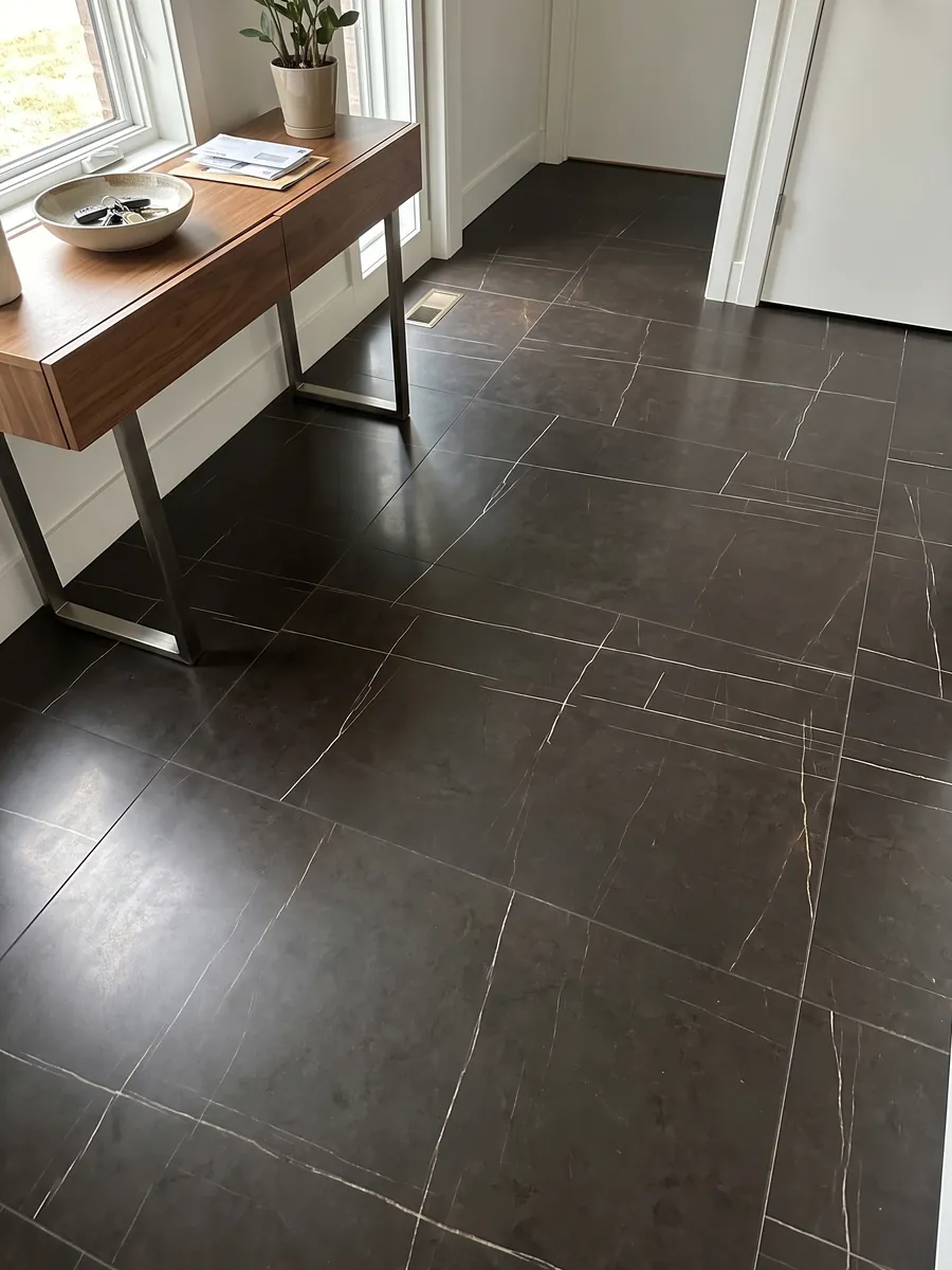 Piso de recibidor en placas grandes de mármol negro Sahara Noir con luz natural: negro amarronado con líneas doradas muy finas, rectas y escasas