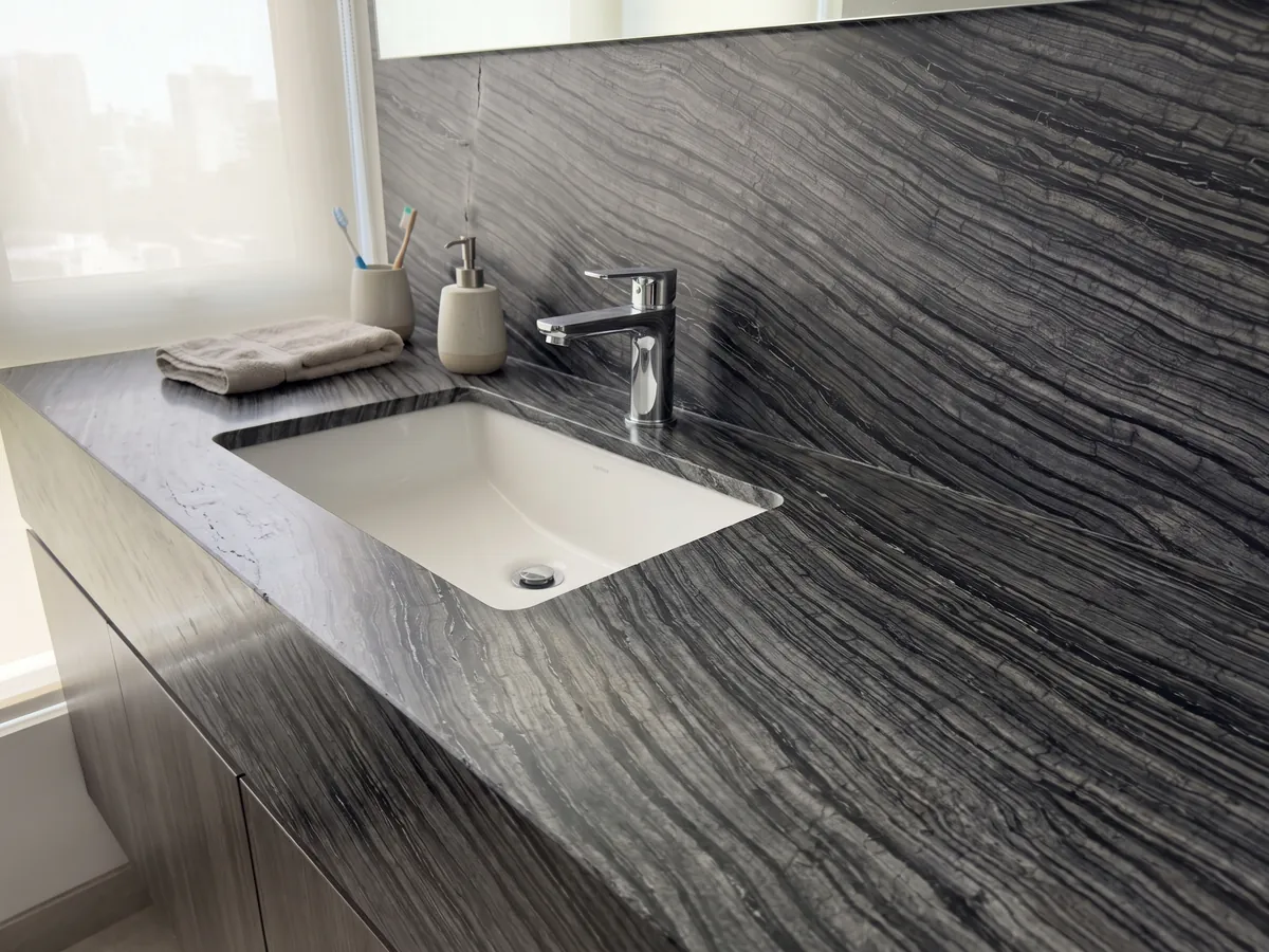 Cubierta de lavabo y pared de baño en mármol negro Zebrato con lavamanos blanco y grifería cromada: negro con rayas finas onduladas grises que corren en diagonal, efecto de corteza