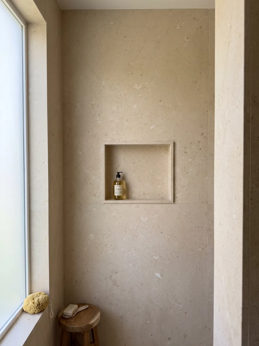 Ducha revestida con placas enteras de Mármol Pietra di Vicenza Blanca con nicho empotrado: beige arena de grano visible, con pequeños fragmentos claros