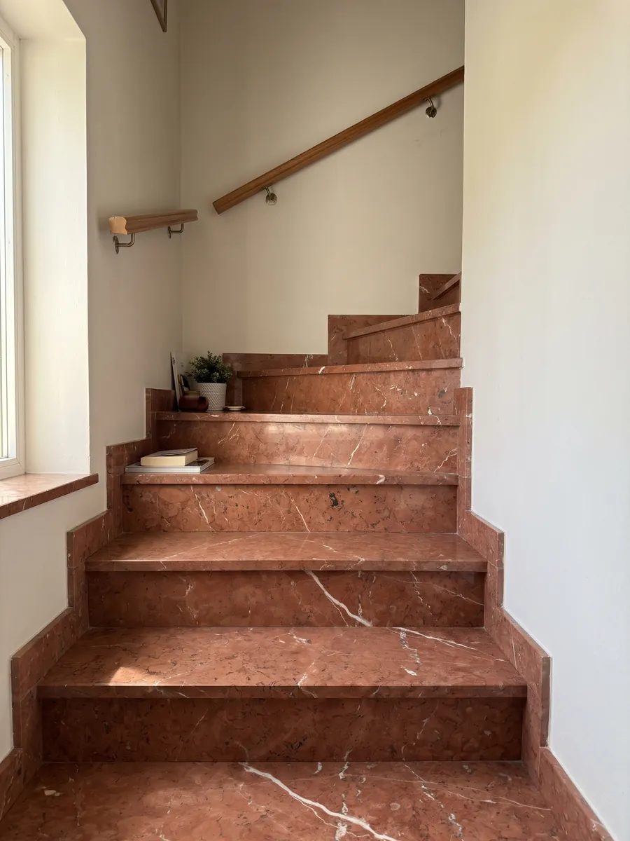 Escalera interior con peldaños de Mármol Rojo Alicante con pasamanos: rojo terracota parejo cruzado por pocas vetas blancas en diagonal