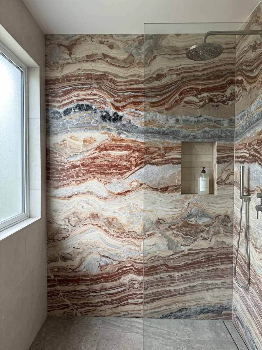 Ducha revestida con placas enteras de mármol rojo Arabescato Rosso con nicho empotrado: bandas horizontales onduladas rojo ladrillo, crema y gris, con manchas negras arriba