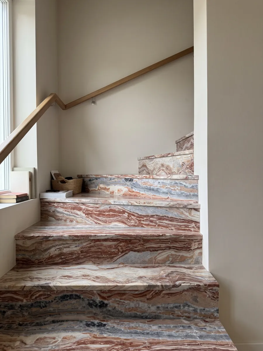 Escalera interior con peldaños de mármol rojo Arabescato Rosso con pasamanos: bandas horizontales onduladas rojo ladrillo, crema y gris, con manchas negras arriba
