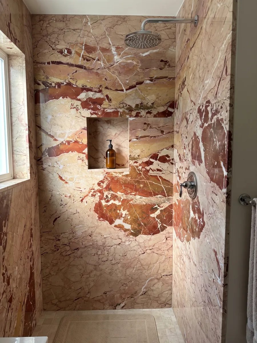 Ducha revestida con placas enteras de mármol rojo Arlecchino con nicho empotrado: grandes manchas rojo óxido sobre beige rosado, cruzadas por vetas blancas finas