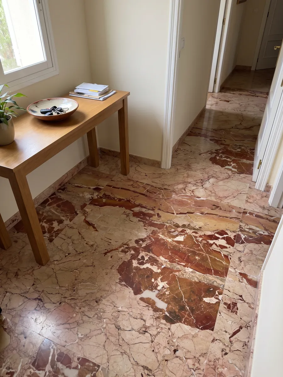 Piso de recibidor en placas grandes de mármol rojo Arlecchino con luz natural: grandes manchas rojo óxido sobre beige rosado, cruzadas por vetas blancas finas