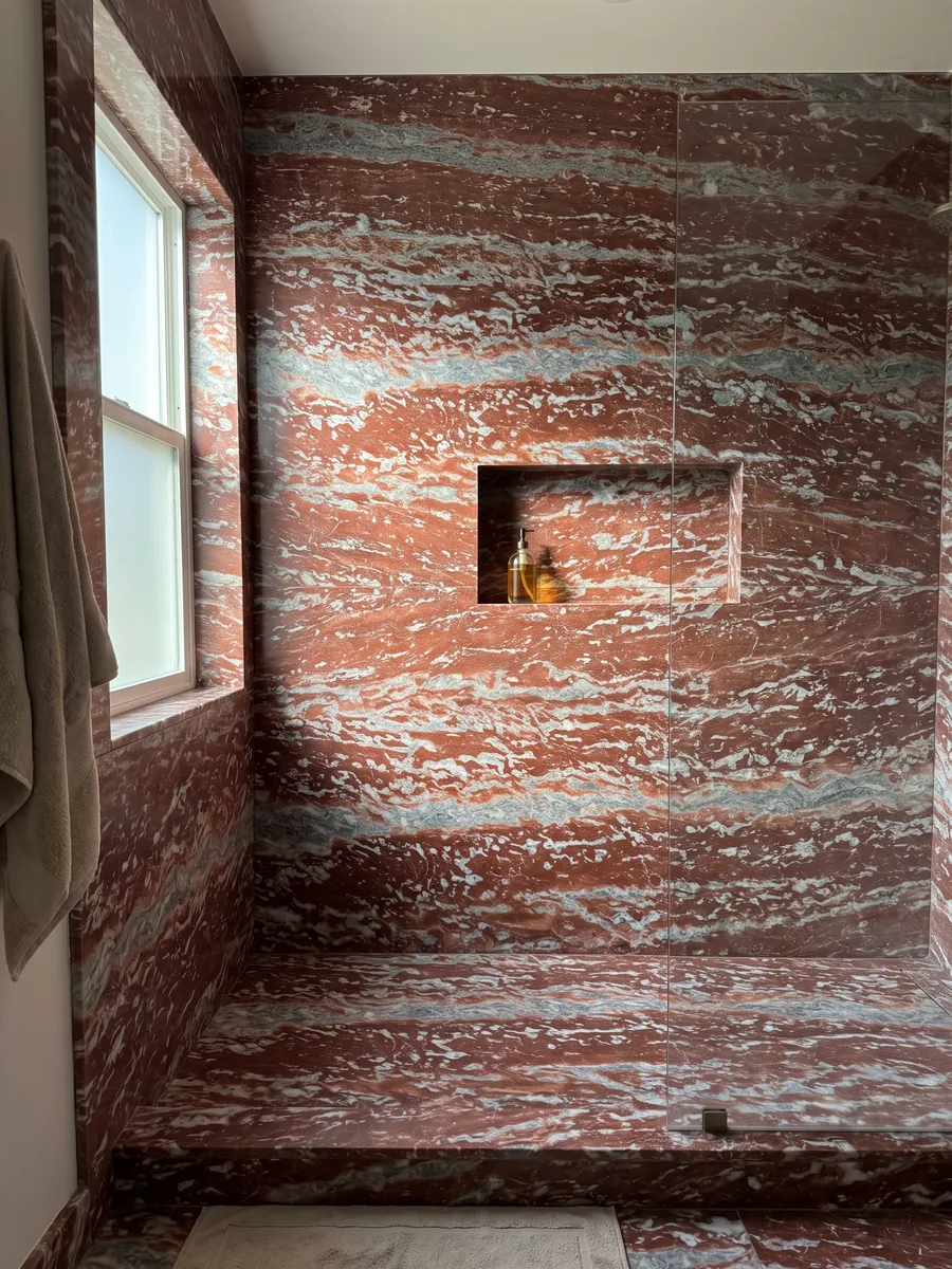 Ducha revestida con placas enteras de Mármol Rojo Francia con nicho empotrado: franjas horizontales rojas que alternan con bandas gris azulado y blancas