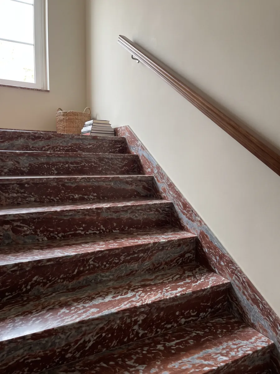 Escalera interior con peldaños de Mármol Rojo Francia con pasamanos: franjas horizontales rojas que alternan con bandas gris azulado y blancas