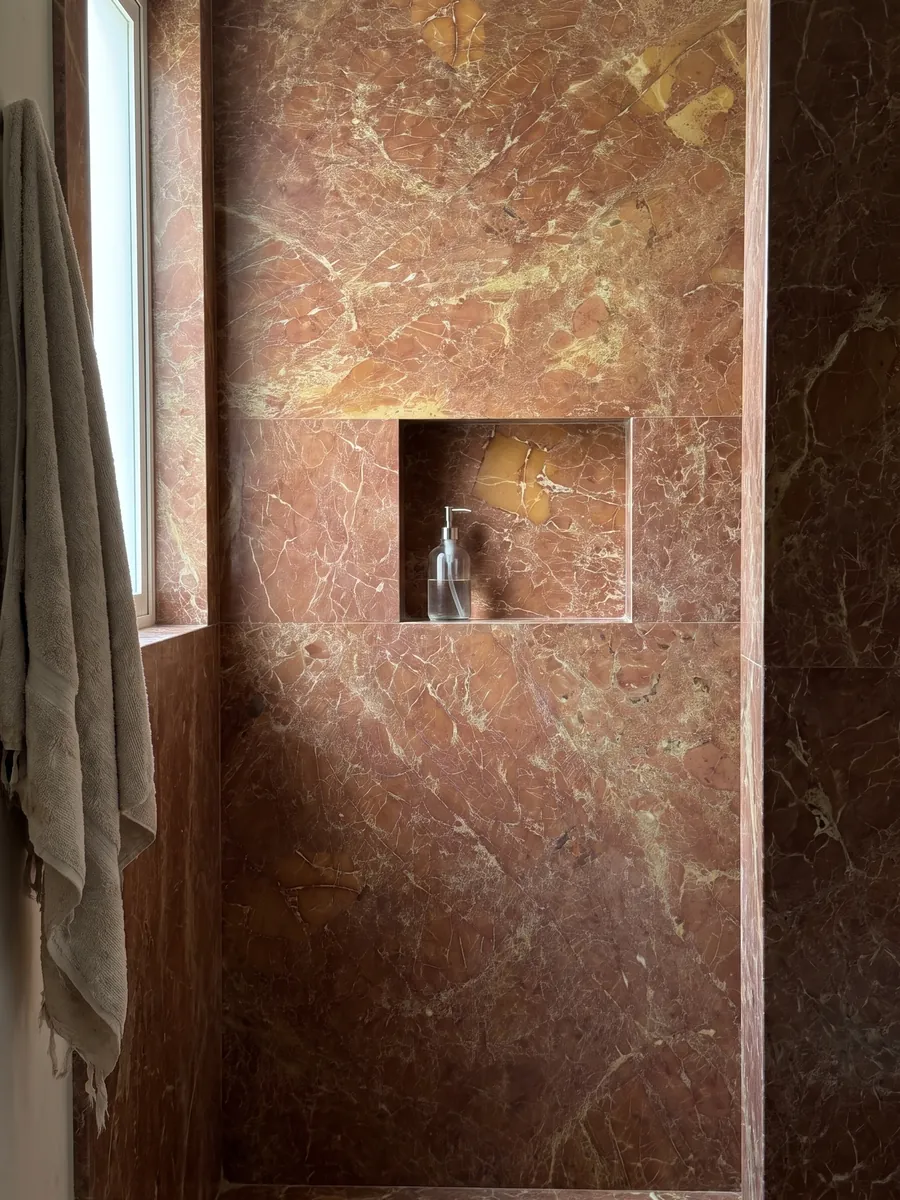 Ducha revestida con placas enteras de mármol rojo Melograno con nicho empotrado: rojo ladrillo amarronado con red fina de vetas claras y zonas ocre