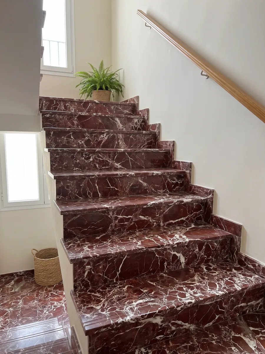 Escalera interior con peldaños de mármol rojo Rosso Lepanto con pasamanos: fragmentos rojo intenso rodeados por una red densa de vetas blancas