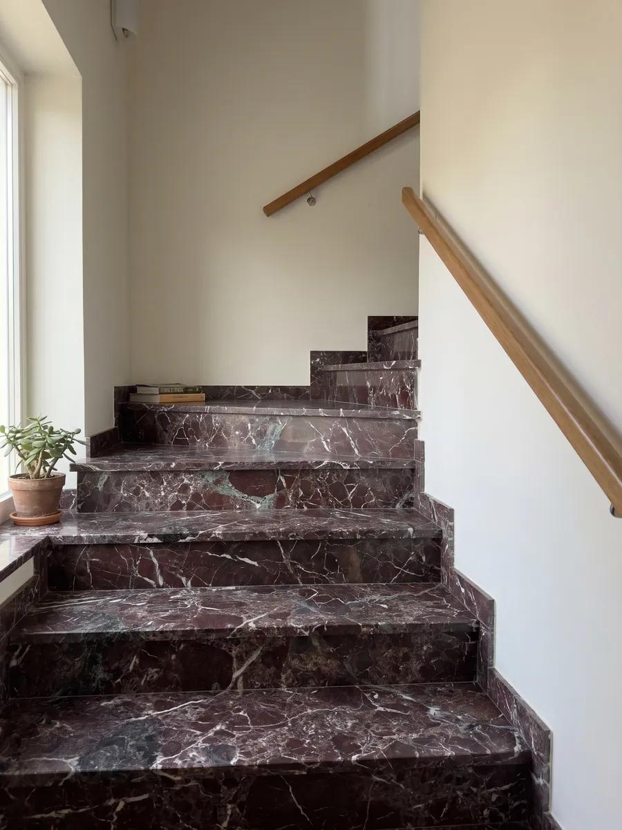Escalera interior con peldaños de mármol rojo Rosso Levanto con pasamanos: burdeos oscuro con zonas verde grisáceo y una red de vetas blancas