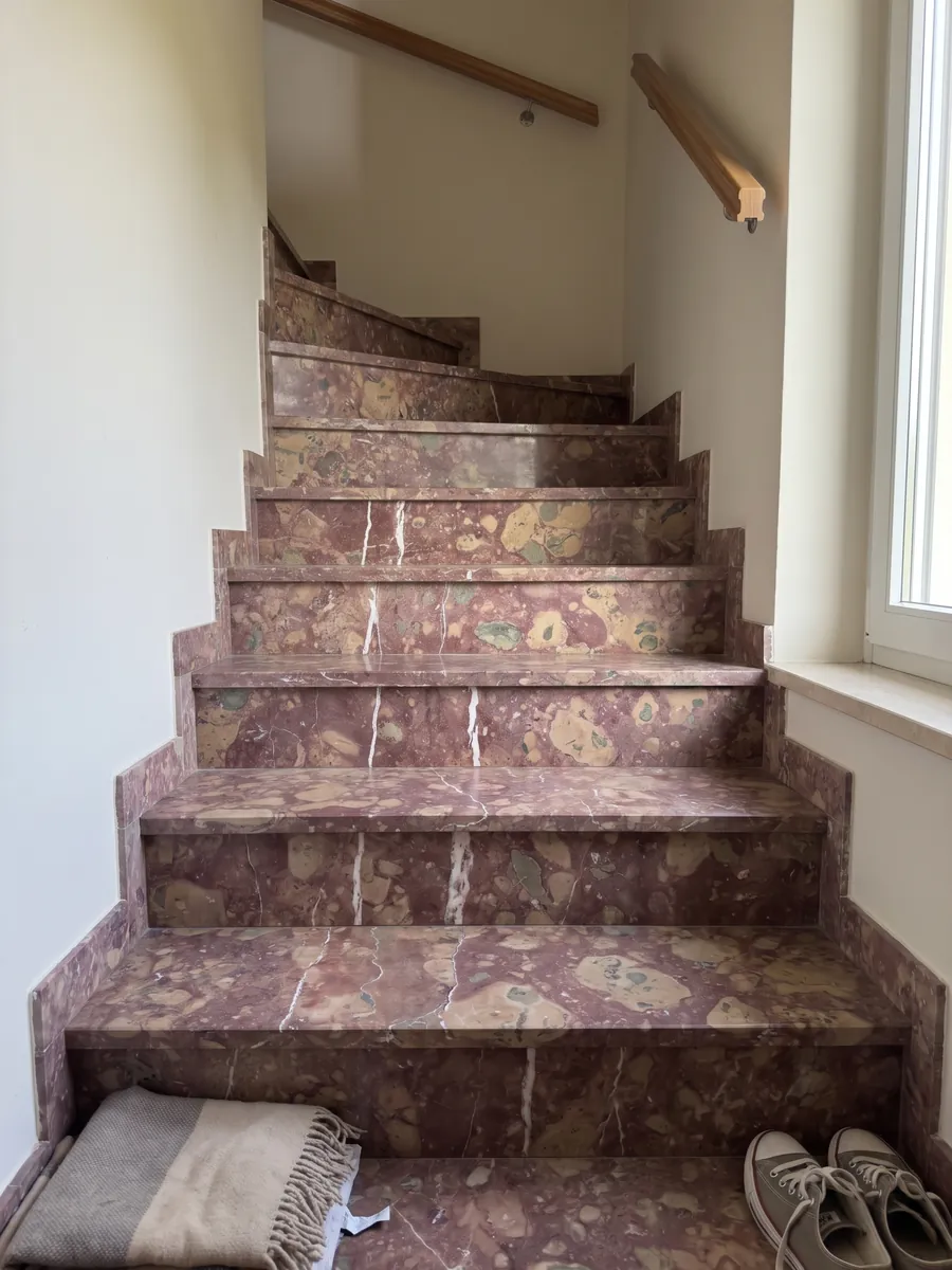 Escalera interior con peldaños de mármol rojo Rosso Verona con pasamanos: rojo violáceo con manchas beige y dos vetas blancas verticales irregulares