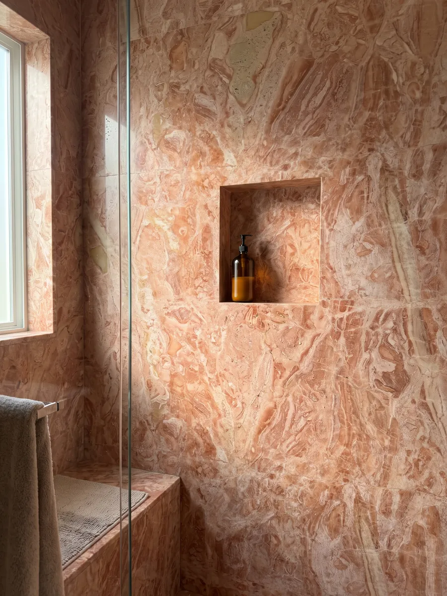 Ducha revestida con placas enteras de mármol rosa Breccia Bohemien con nicho empotrado: mezcla densa de fragmentos coral y beige claro en tonos salmón