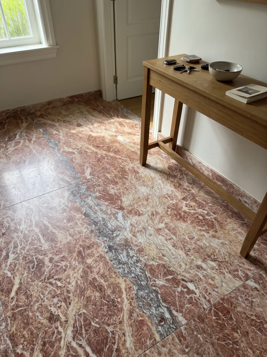 Piso de recibidor en placas grandes de Mármol Rosa Peralba con luz natural: rosa rojizo con red de vetas blancas y una franja vertical gris violácea