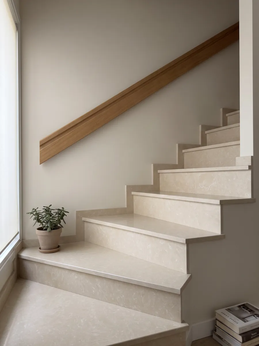 Escalera interior con peldaños de Mármol Sintético Ecrù con Resina con pasamanos: superficie crema lisa y homogénea, casi sin dibujo