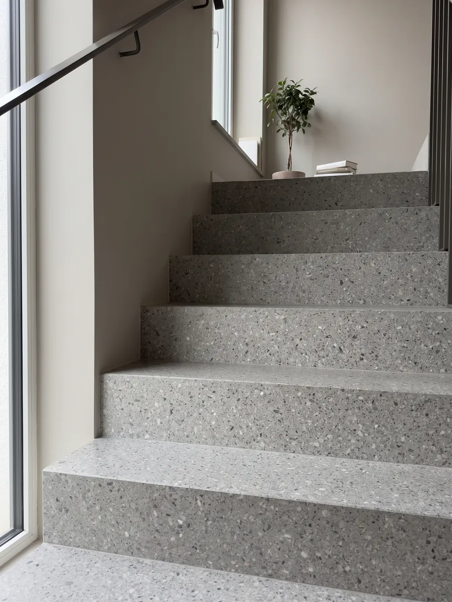 Escalera interior con peldaños de Mármol Sintético Fior di Pesco Grey con Cemento con pasamanos: gris medio con pequeños fragmentos blancos y oscuros, estilo terrazo fino