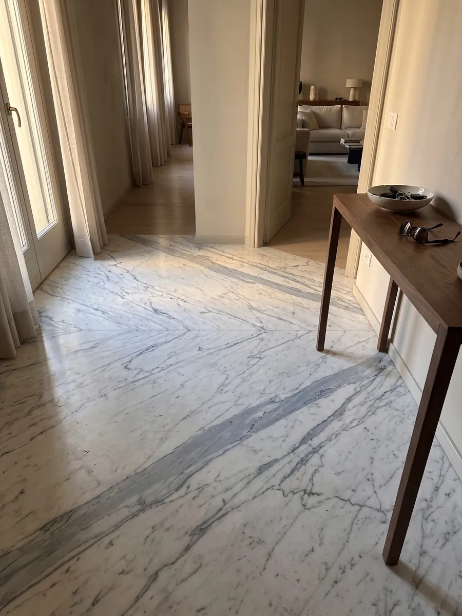 Piso de recibidor en placas grandes de Mármol Statuarietto con luz natural: blanco con vetas gris azulado en diagonal