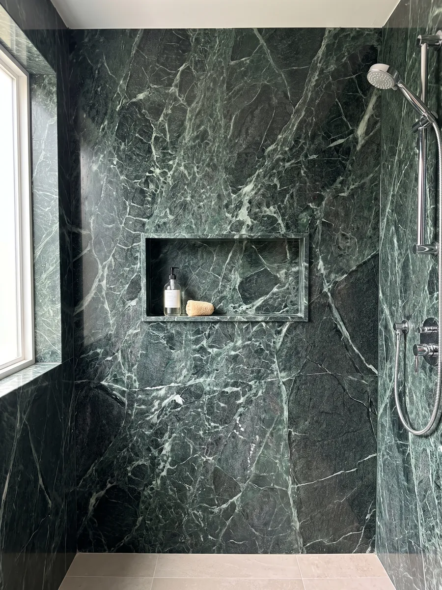 Ducha revestida con placas enteras de Mármol Verde Alpi con nicho empotrado: verde casi negro atravesado por una red tupida de vetas verde claro y blancas