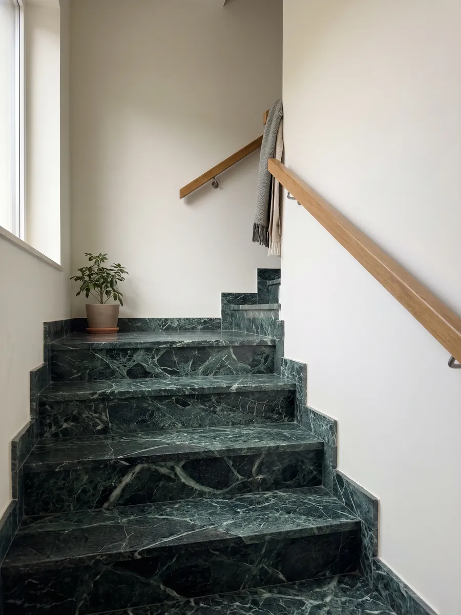 Escalera interior con peldaños de Mármol Verde Alpi con pasamanos: verde casi negro atravesado por una red tupida de vetas verde claro y blancas