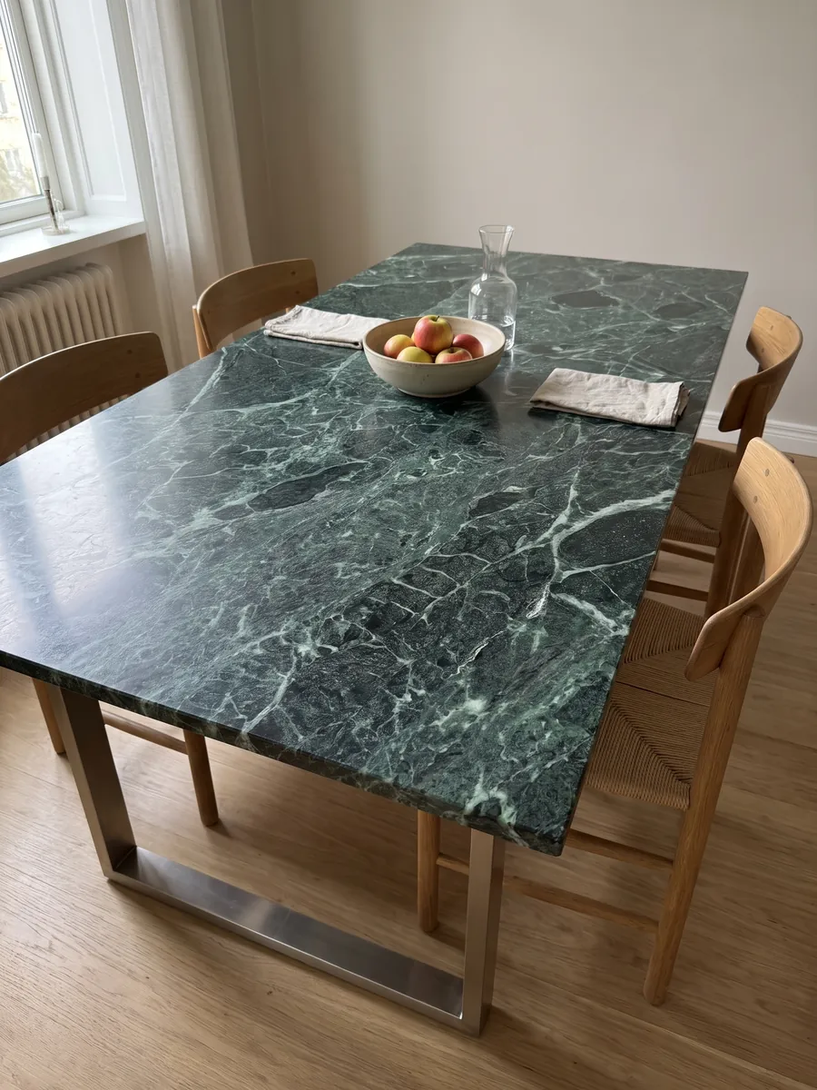 Mesa de comedor con cubierta de Mármol Verde Alpi sobre base de acero: verde casi negro atravesado por una red tupida de vetas verde claro y blancas