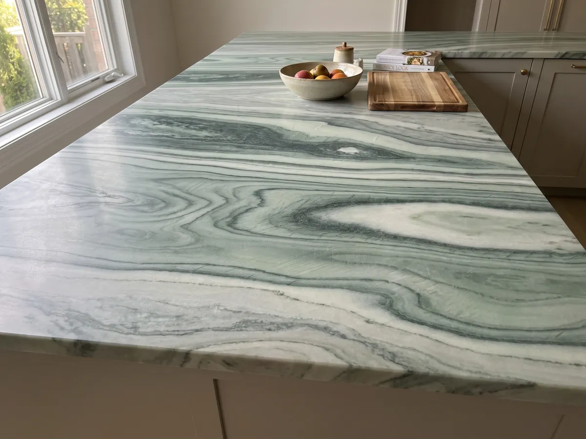 Isla de cocina con cubierta de mármol verde Cipollino y canto recto en una cocina con luz natural: bandas onduladas verde oscuro y claro con forma de ojo en el centro